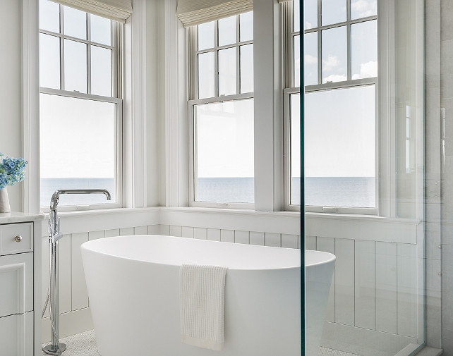 Master bathroom boasts walls clad in vertical shiplap framing windows dressed in cream roman shades situated over a freestanding oval tub and a floor mount spigot tub filler placed next to a seamless glass shower. #Bathroom #Tub #FreestandingBath #FloorMountTubFiller #SpigotTubFiller