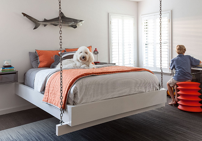 Boys Bedroom. Hanging bed in boys bedroom. Boy's bedroom features a shark sculpture over a hanging bed suspended from the ceiling by chains dressed in gray and orange bedding flanked by floating industrial metal nightstands. #BoysBedroom #HangingBed Jean Liu Design.