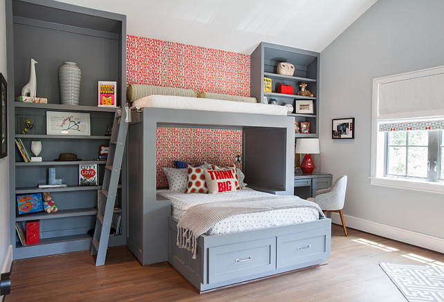 Built-in Bed with reading lounge on top. Gray kid's bedroom features a wall clad in red alphabet wallpaper lined with a gray bed dressed in gray polka dot bedding situated under an overhead reading nook accessible by a gray ladder. Contemporary boy's bedroom features a built-in bed flanked by floor to ceiling gray bookcases with the right bookcase fitted with a gray desk and a striped task chair. Wallpaper is Alexander Girard Alphabet wallpaper manufactured by Maharam. Laura U, Inc.