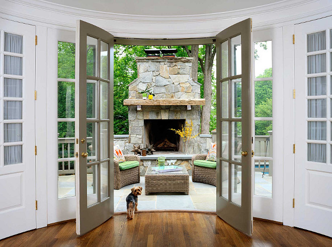 Patio Stone Fireplace and Hearth. French Doors open to a patio with natural stone fireplace and hearth. French doors open to a patio filled with a stone fireplace with hearth alongside a pair of wicker chairs with green cushions facing each other across from a wicker ottoman with glass top. #Patio #StoneFireplace #Hearth Erica Burns Interiors.