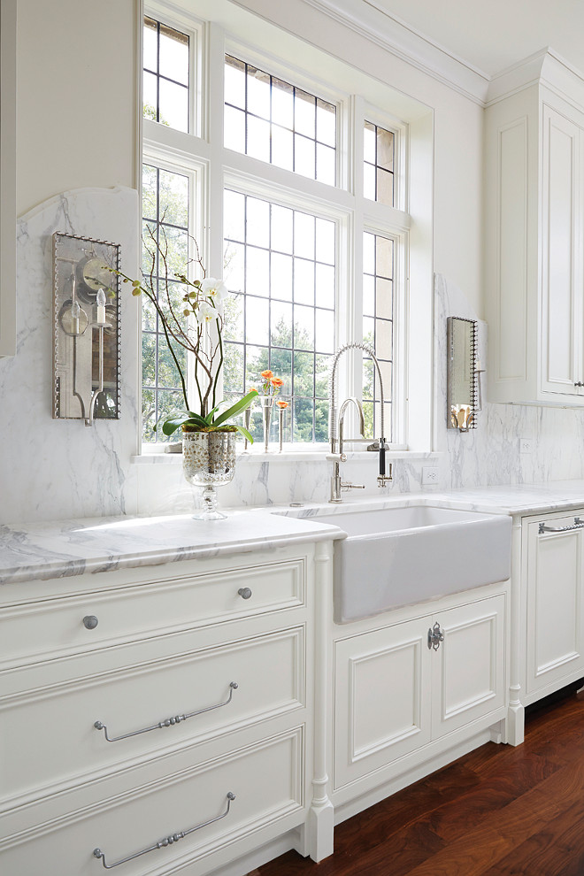 Kitchen Sink Windows and Sconces. Kitchen with sconces. Kitchen farmhouse sink, industrial faucet and mirrored sconces. Exquisite kitchen features creamy white cabinets paired with grey and white marble countertops and a curved marble backsplash lined with mirrored wall sconces. A farmhouse sink and pull out faucet stands below windows. #Kitchen #Sconces #FarmhouseSink Cyndy Cantley.