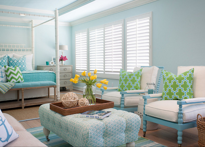 Turquoise Bedroom sitting area is filled with a pair of blue spindle chairs lined with green and blue Moroccan tile pillows facing a blue tufted ottoman on caster legs atop a turquoise and green striped rug. #Turquoise #Bedroom AGK Design Studio.