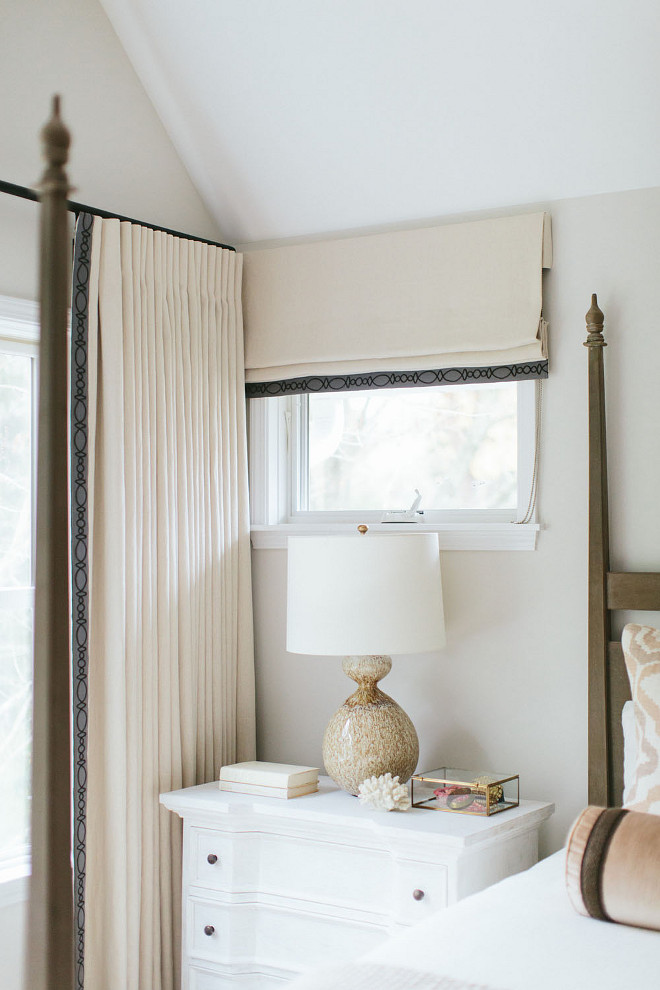 Neutral bedroom with whitewashed nightstand and a brown lamp, Aerin Gannet Lamp, placed under a window dressed in a cream roman shade. Kate Marker Interiors