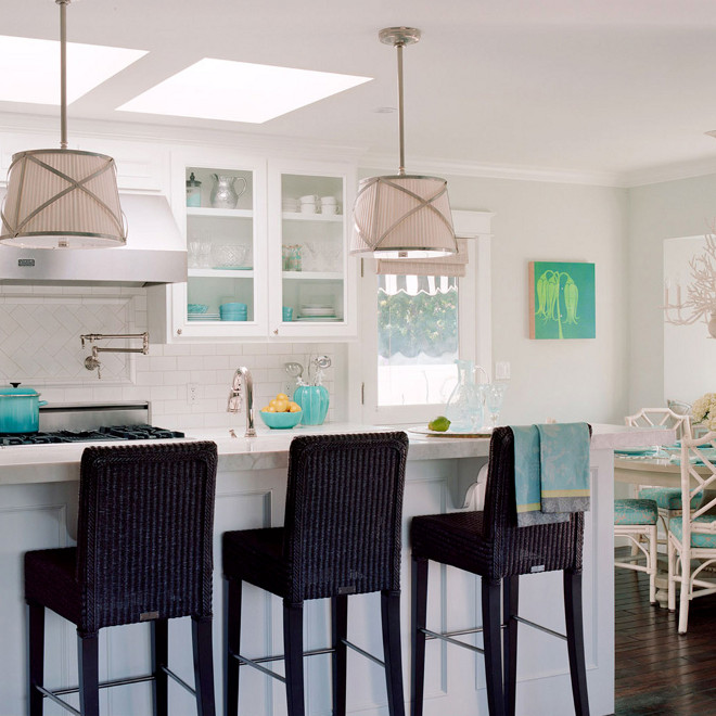 White and turquoise kitchen, Lovely airy beachy coastal kitchen design with soft gray walls, chrome pleated drum pendant island lights, black seagrass barstools, white kitchen cabinets, subway tiles, white faux bamboo dining chairs, turquoise blue striped chair cushions, white chandelier and turquoise blue accents #Kitchen #BeachhouseKitchen #CoastalKitchen #WhiteandturquoiseKitchen Waterleaf Interiors