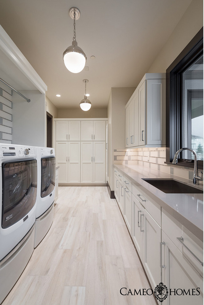 Laundry room with white cabinets, gray quartz countertop, wood grain ceramic tiles and walls painted in Pale Oak by Benjamin Moore. Laundry Room #Laundryroom Cameo Homes Inc.