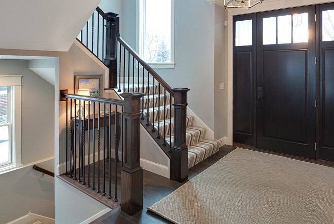 Front entry foyer with dark stained wood door, dark stained hardwood floors, dark stained staircase railing and newel post. Grace Hill Design