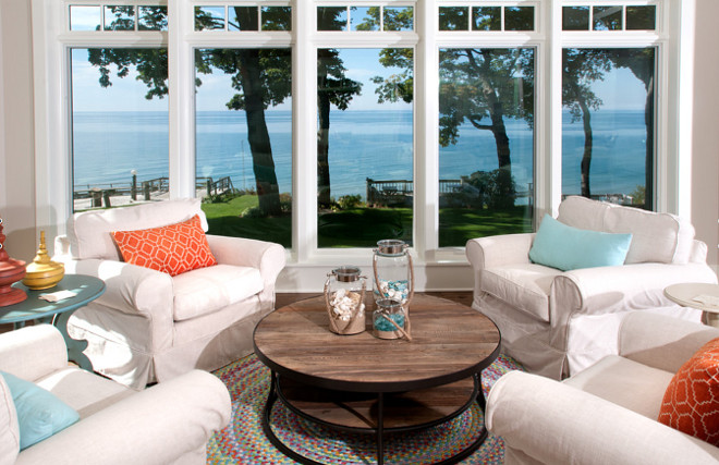 Coastal living room. Lake views can be seen through 8-foot tall windows in the sitting area of the living room. Vivid pops of color appear throughout as seen in this comfy lounging area that provides a perfect spot to watch the sunset over the lake. Coastal homes. Coastal interiors. #coastal #coastalLivingroom #CoastalInteriors #CoastalHomes 
