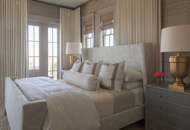 Small Bedroom. This chic small bedroom features a light gray wingback bed dressed in white and gray bedding as well as gray Greek key border pillows flanked by dark gray bamboo nightstands and Large Chunky Urn Table Lamps in Antique Burnished Brass. Windows are dressed in ivory curtains layered over bamboo roman shades. #Smallbedroom #Chicsmallbedroom #bedroom Urban Grace Interiors