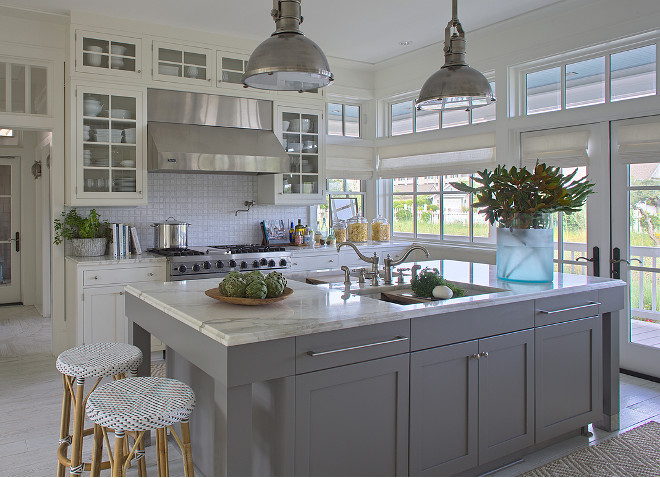 White kitchen with gray island. This white and gray kitchen features Chart House 1 Light Country Industrial Pendants in Antique Nickel with Large Antique Nickel Shades. The bistro barstools are Serena & Lily Riviera Backless Stools. The back of the kitchen boasts white glass-front cabinets surrounding a stainless steel kitchen hood over swing-arm pot filler over stainless steel stove beside windows and French doors under transom windows. White kitchen cabinet with gray island. White and gray kitchen #Whitekitchen #Grayisland #whiteandgraykitchen #whitecabinets #grayisland #kitchen Urban Grace Interiors.