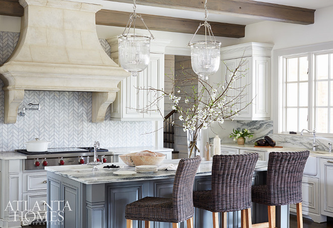 Kitchen. The kitchen juxtaposes varying textures rather than contrasting colors. The carrara marble backsplash, laid in herringbone pattern next to the Limestone hood, wooden beamed celing, and veiny Vermont marble countertops, bring a soft, subtle contrast to the space. Kitchen Limestone Hood & Herringbone Backsplash #kitchen. Amy Meier for Atlanta Homes & Lifestyles. 