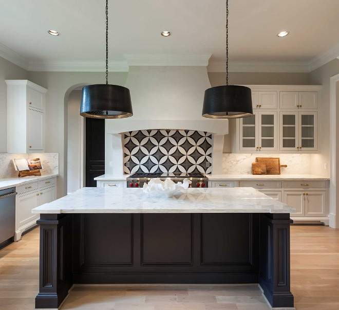 Kitchen. Black and white kitchen features white cabinets adorned with brass hardware paired with white marble countertops and backsplash. A white kitchen hood with corbels stands over a black and white circle tile backsplash, Cement Tile Shop Circle Tile, and a Wolf range. A pair of black drum pendants, Arteriors Anderson Iron Pendants, illuminates a black kitchen island topped with contrasting white marble. Elizabeth Garrett Interiors