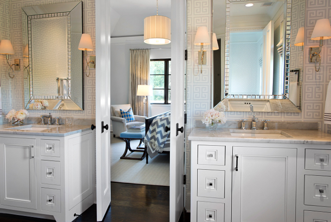 Bathroom. This master bathroom looks even more elegant with these bi-fold doors and the dark hardwood floors. Large beveled mirrors are flanked by Waterworks Blue Note Wall Mounted Single Arm Sconces with Cone Shades over white vanities with white carrara marble countertops. #bathroom #vanity #carrara #marble #hardwood #flooring #sconces TS Adams Studio Architects. Traci Rhoads Interiors.