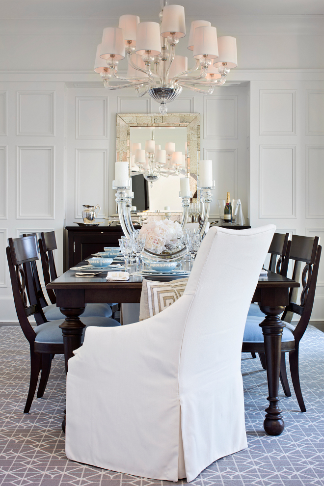 Dining room. Dining Room Wainscoting. Sophisticated dining room with full wall wainscoting framing antiqued mirror over espresso buffet. Glamorous chandelier sits above rectangular espresso dining table lined with espresso dining chairs with blue velvet cushions and white slipcovered captain dining chairs over gray geometric rug layered over espresso wood floors. #Diningroom #Wainscoting #diningroom #wainscotingwalls #wainscotting #millwork TS Adams Studio Architects. Traci Rhoads Interiors. 