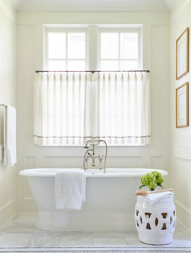 Bath nook wainscotting. Bath nook is clad in decorative wall moldings filled with a roll top tub and a vintage hand held tub filler as well as a white rope stool placed under windows dressed in white sheer cafe curtains accented with gray trim. #bathnook #nook #wainscotting Sarah Bartholomew Design