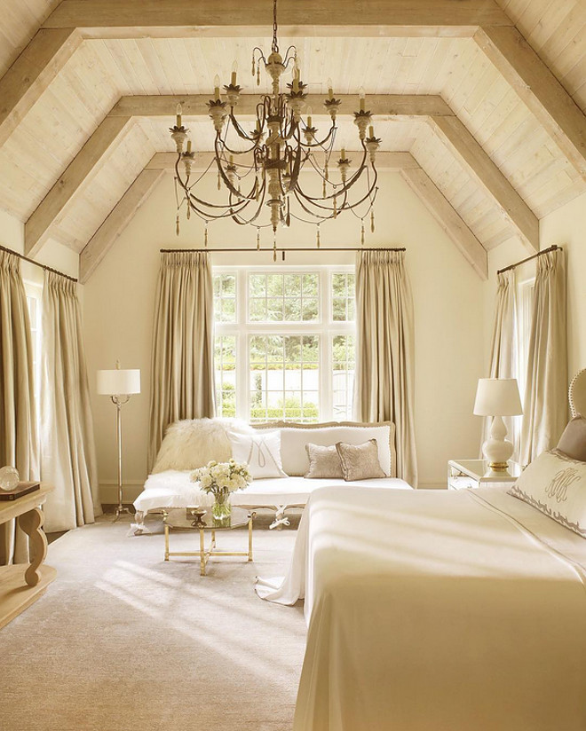 A vaulted oak ceiling and antique chandelier give this bedroom, designed by Suzanne Kasler, a warm feel.