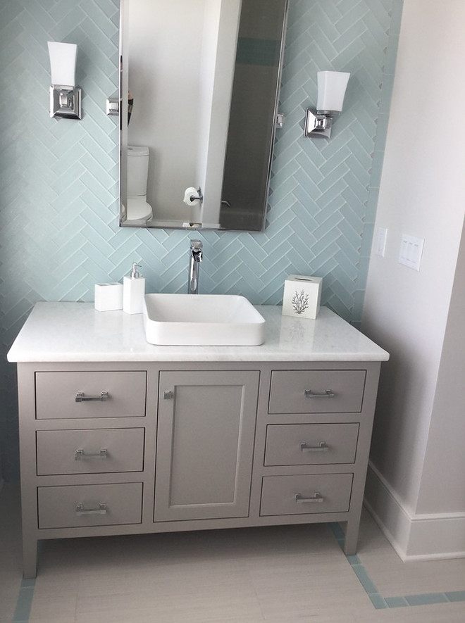 Bathroom. This bathroom features floor-to-ceiling subway tile in a herringbone pattern. The vanity is painted vanity in a soft gray - Sherwin Williams SW7023 Requisite Gray. Subway tile is in a herringbone pattern. Painted vanity in a soft gray. Walls: Sherwin Williams Anew Gray & 3x6 Capricco sky blue glass tile in 3x6 herringbone pattern. Countertop is Silestone Quartz – White Storm. The Guest House Studio