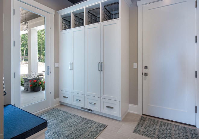 Mudroom. Garage door opens to a mudroom with tile floors, closed cubbies with doors and a small built-in bench. #mudroom #door #cubbies #floortile #tile
