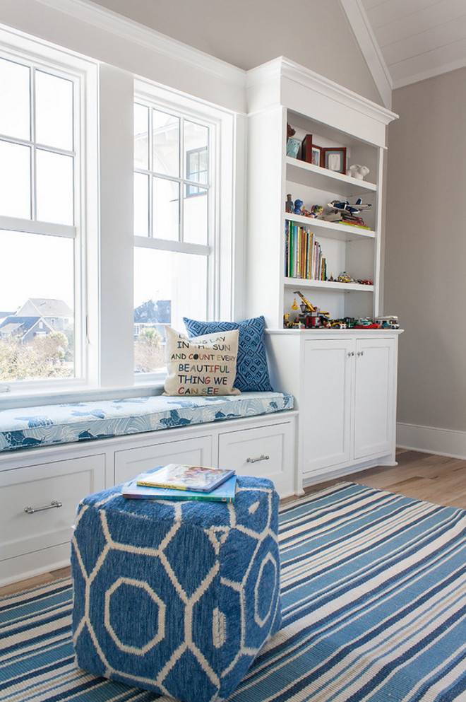 Window seat flanked by built-in cabinets with bookcases, blue striped rug and blue and white ottoman and pillows. Cabinet paint color is Sherwin Williams SW7006 Extra White. The Guest House Studio