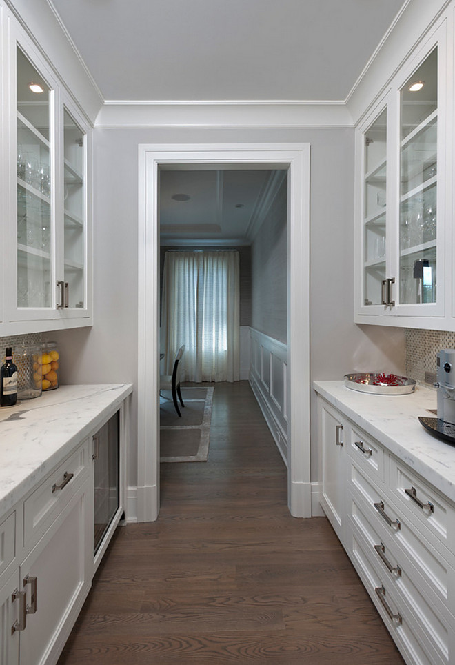 Butlers pantry by dining room. The formal dining room with paneling and tray ceiling is serviced by a custom fitted double-sided butler’s pantry with hammered polished nickel sink and beverage center. #butlerspantry #diningroom #countertop #beveragecenter Bluewater Home Buildersutlers-pantry