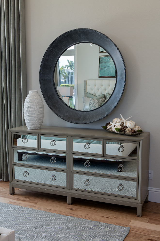 Mirrored Dresser. Bedroom Dresser. Bedroom mirrored dresser. A large round mirror with a wide dark metal frame hangs above a mirrored dresser, which showcases an assortment of coastal accessories such as starfish and seashells. #bedroom #dresser #mirroreddresser