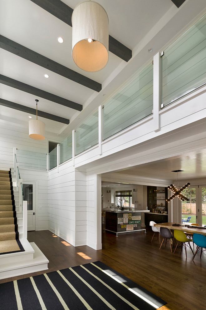 East coast style modern farmhouse foyer. Modern farmhouse foyer. East coast style modern farmhouse two story entry foyer with gray wood beamed ceiling beautifully contrasting with modern glass balustrade in the second story balcony and bright white random width shiplap paneling. #modernfarmhouse #entry #foyer #eastcoaststyle #shiplap Bluewater Home Builders