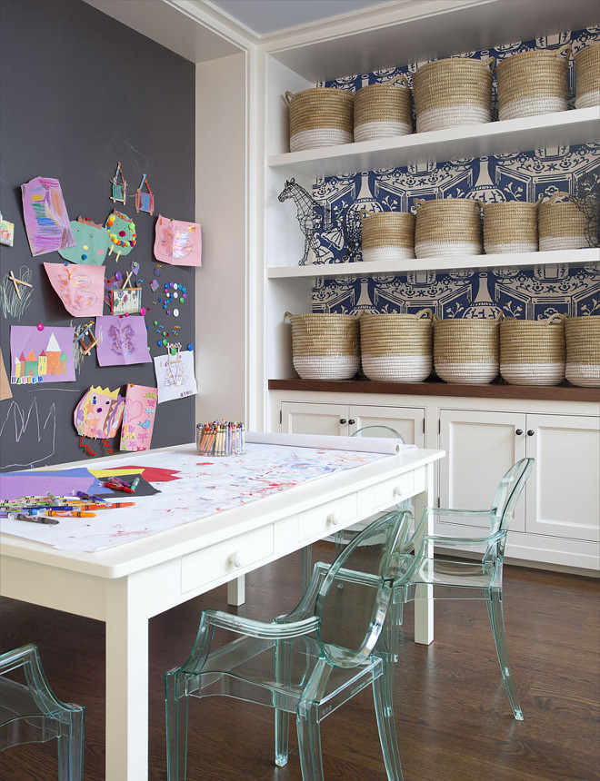 Playroom Chalk Wall. Kids playroom boasts a chalkboard accent wall placed in front of a white play table with drawers lined with Kartell Lou Lou Ghost Chairs in across from alcove clad with white and blue vase wallpaper, David Hicks The Vase Wallpaper, lined with white floating shelves filled with white dipped baskets over built in cabinets topped with wood countertop. #kidsplayroom #playroom #chalk #chalkwall Anik Pearson Architect