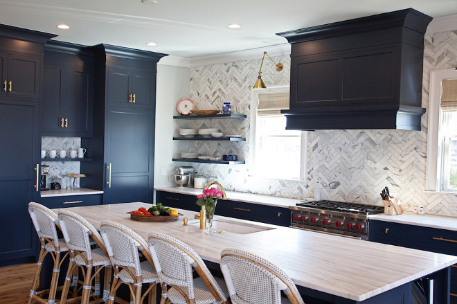 Benjamin Moore Hale Navy Kichen with Brass Accents. This navy kitchen, features an eye-catching navy blue kitchen island is fitted with gray and white quartzite countertops holding an undermount sink with a brass gooseneck facuet and seating five Serena & Lily Riviera Counter Stools. The island faces a wall covered in herringbone marble backsplash tiles holding three floating navy shelves and framing windows covered in bamboo roman shades flanking a navy hood hung over a Wolf range mounted in navy shaker cabinets completed with brass pulls illuminated by brass wing arm sconces. The remaining wall boasts a navy blue paneled double fridge separated by a cafe station and positioned under more navy blue cabinets in Benjamin Moore Hale Navy.benjamin-moore-hale-navy-kichen-with-brass-accents Benjamin Moore Hale Navy Kichen with Brass Accents. #BenjaminMooreHaleNavy #Kichen #Brass Accents Stonington Cabinetry
