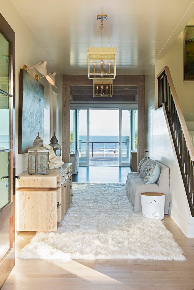 Coastal Foyer. This stunning coastal foyer feature shiplap paneled walls and ceiling with glass doors to an open ocean view. #Foyer #coastalfoyer #shiplap #paneling #shiplapwalls #shiplapceiling Herlong & Associates Architects + Interiors