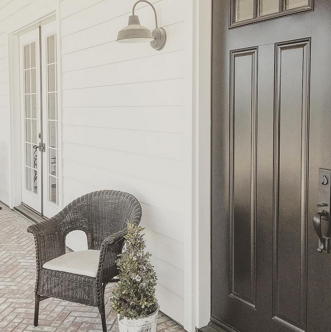 The farmhouse porch features white siding painted in Sherwin Williams Pure White, black door painted in Sherwin Williams Tricorn Black and reclaimed brick flooring. farmhouse-front-porch-with-black-front-door-and-reclaimed-brick-flooring #farmhouse #porch #frontporch #paintcolor #SherwinWilliamspurewhite #SherwinWilliamsTricornBlack Home Bunch's Beautiful Homes of Instagram ourfarmhousefit