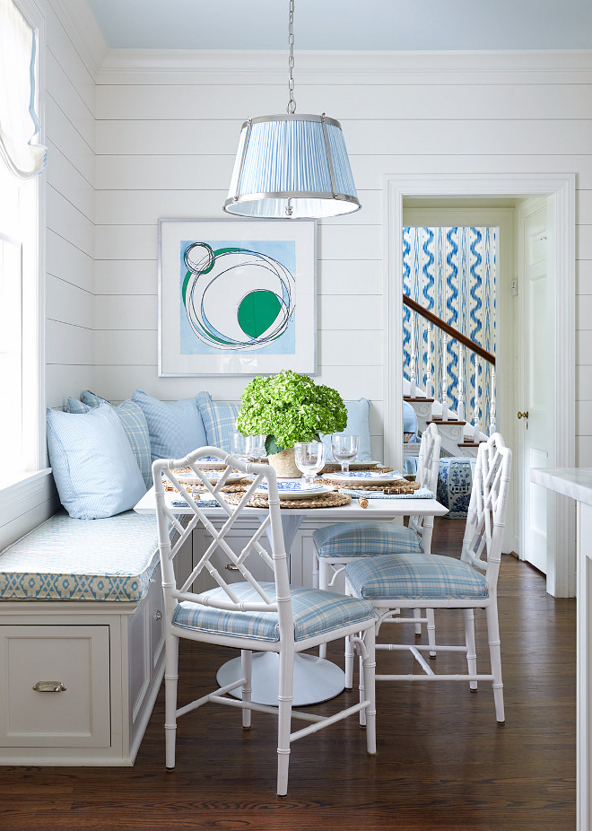 Shiplap White and Blue Breakfast Room with White Bamboo Chairs. Blue and white breakfast room features a blue Vaughn Nickel Hanging Shade Pendant hung from a blue ceiling over a square white dining table seating three white bamboo chairs accented with blue plaid seat cushions complementing blue plaid and solid blue pillows placed atop an L-shaped dining bench adorning polished nickel cup pulls and a blue trellis cushion positioned beneath a window dressed in a white roman shade. The space is completed with a blue and white print mounted above the bench on a shiplap wall. shiplap #Shiplap #WhiteandBlue #BreakfastRoom #WhiteBambooChairs Sarah Bartholomew Design
