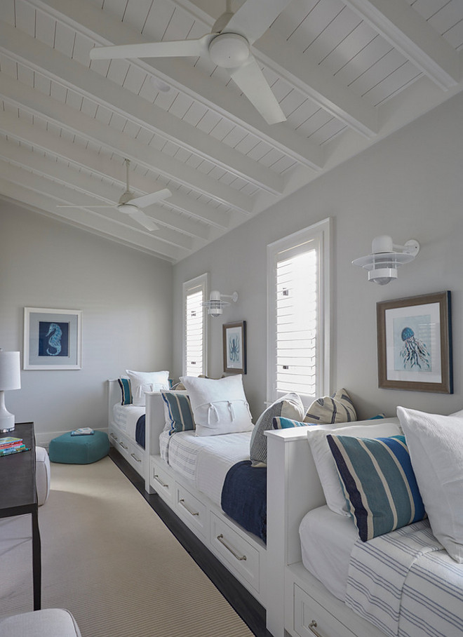 Benjamin Moore Classic Gray. The kids' bedroom feature a row of white built-in beds fitted with storage drawers dressed in white and blue striped bedding and pillows lining a single gray wall illuminated by white nautical wall sconces. A shiplap sloped ceiling accented with white modern ceiling fans hover over a wall of twin built-in beds tucked under windows. . Bedroom paint color is Benjamin Moore Classic Gray. Benjamin Moore Classic Gray #BenjaminMooreClassicGray benjamin-moore-classic-gray