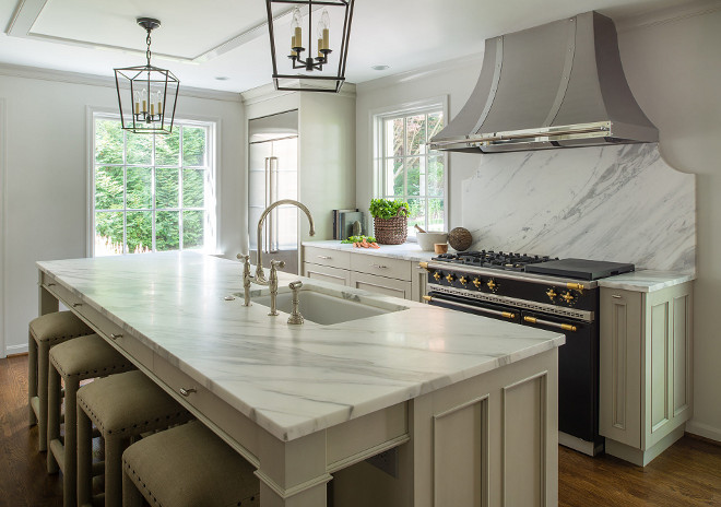 Classic Kitchen Design. Classic Kitchen Design with soft gray cabinets, large kitchen island with white and gray honed marble countertop, tow pairs of Darlana pendants. This classic kitchen design also features a stainless custom hood and marble slab backsplash. #ClassicKitchenDesign ClassicKitchen #kitchen #kitchenDesign Anthony Wilder. John Cole Photography.