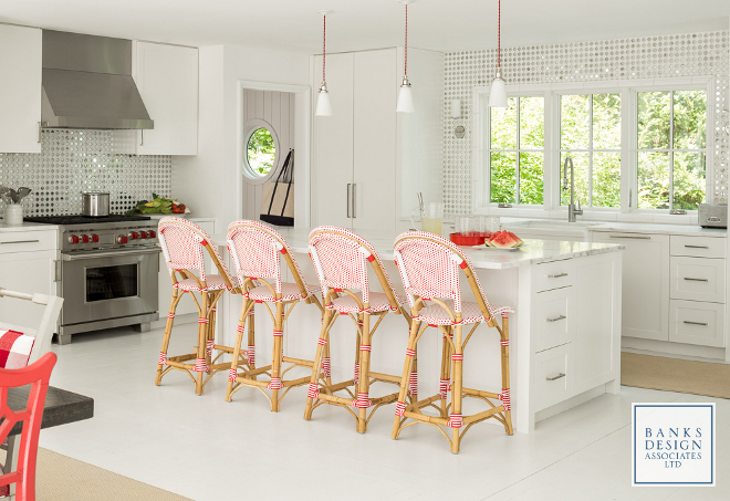 White kitchen with pops of color. White kitchn pops of color ideas. Red, the homeowner's favorite color, is brought to the kitchen through the rattan French bistro barstools and pendants. Red pendants are Rejuvenation McCoy, brushed nickel. Floors are existing, painted Benjamin Moore Decorator White. #whitekitchen #color Banks Design Associates, LTD & Simply Home