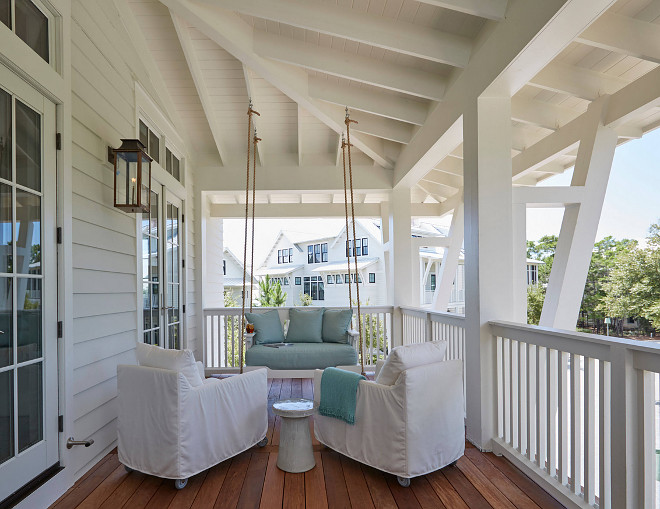 Porch Swing. White and turquoise porch swing. Beach Home Porch with Rope Swing. Beach home porch features a rope swing sofa adorned with blue cushions facing a pair of white slipcovered chairs. #porch #porchswing #ropeswing Geoff Chick & Associates porch-swing-white-and-turquoise-porch-swing