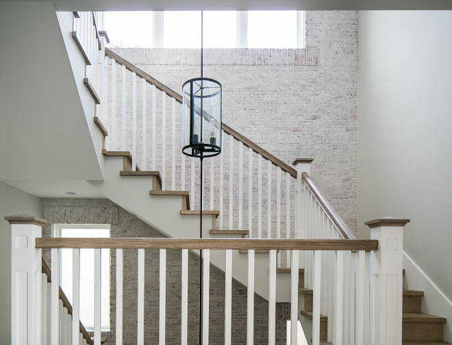 Farmhouse Staircase. Farmhouse staircase. This stairwell packs a serious dramatic punch with its mixed use of materials...including a whitewashed brick wall, stain grade white oak handrail, and custom made brass, three-story chandelier with a pendant at each of the floor's landings. #Farmhousestaircase
