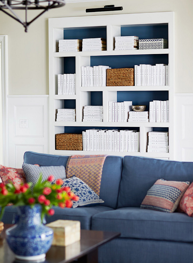Bookcase painted in navy. The living room also features a white bookcase with back painted in navy, and decorated with woven baskets and white books. #Bookcase #navypaintcolor #whitebooks #bookcasetyling Andrew Howard Interior Design
