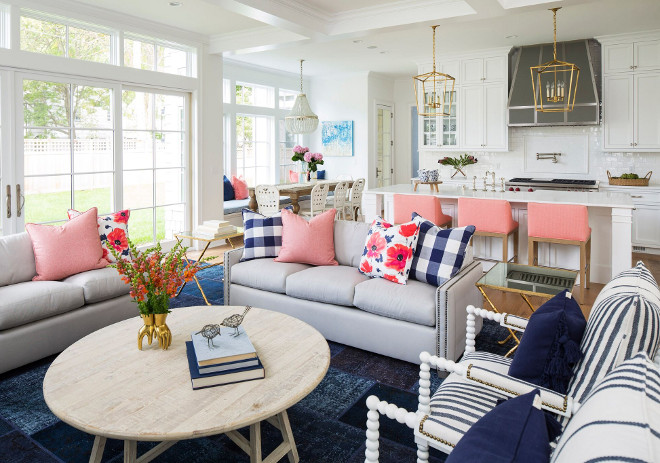 This gray and blue living room features a light gray sofa accented with nailhead trim and blue buffalo check pillows and pink and blue floral pillows. Living room with navy blue rug, open layout, round coffee table, French doors and transoms, pink pillows, checkered pillows and floral pillows #Livingroom #navybluerug #openlayout #roundcoffeetable #Frenchdoors #transoms #pinkpillows #checkeredpillows #floralpillows Martha O'Hara Interiors. John Kraemer & Sons