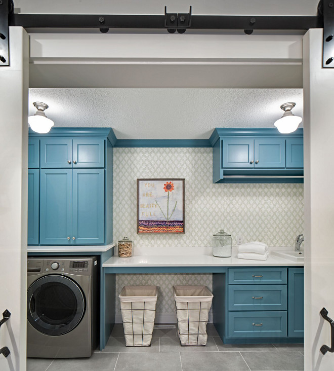 Laundry room with barn doors, blue cabinets, metal laundry hampers and wallpaper The wallpaper is Thibaut wallpaper - Bonaire T88755 Color Green on White #Laundryroom #barndoors #Bluecabinets #metallaundryhampers#laundrybaskets #wallpaper Grace Hill Design