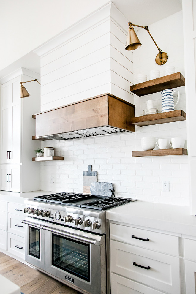 Farmhouse Kitchen Brick Backsplash Chunky Floating Open Shelves and Shiplap Hood. The white shiplap kitchen hood got a dose of stained wood and the open shelving was made of stained wood as well. The warm wood elements pop against the white shiplap and painted brick backsplash. Farmhouse Kitchen Brick Backsplash Chunky Floating Open Shelves and Shiplap Hood. Farmhouse Kitchen Brick Backsplash Chunky Floating Open Shelves and Shiplap Hood #FarmhouseKitchen #BrickBacksplash #ChunkyFloatingOpenShelves #ChunkyShelves #FloatingOpenShelves #ShiplapHood #Shiplap Sita Montgomery Interiors