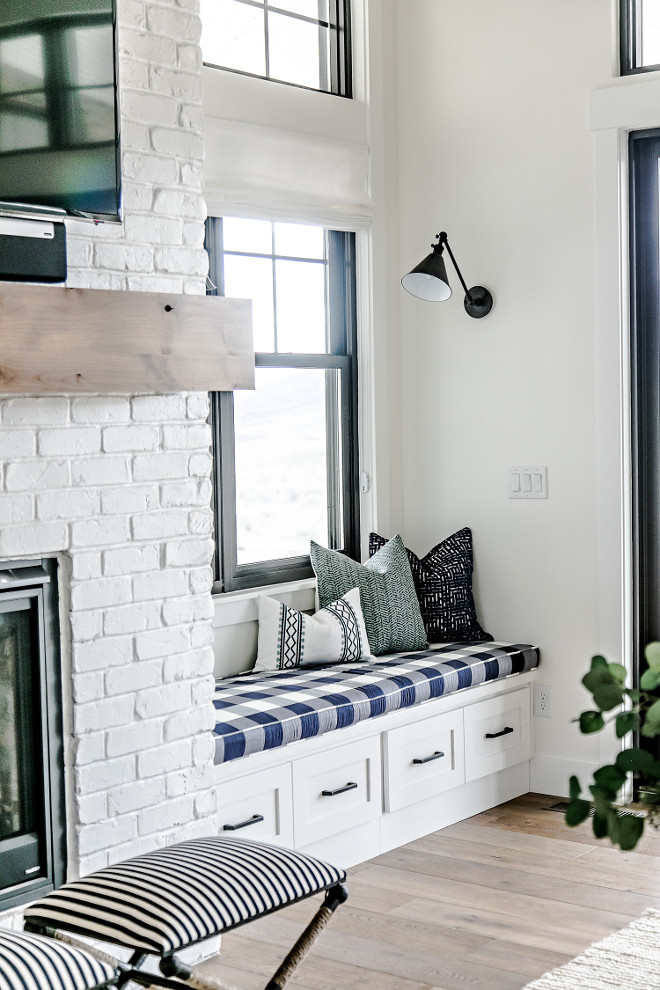 Farmhouse Reading Nook. Farmhouse Window Seat Reading Nook. The window seat is the perfect spot to sit and gaze at the gorgeous view or curl up with a good book. The two library sconces give off the perfect light for the evening hours. The black windows are absolutely stunning against the white interior walls. This bold contrast is my favorite! #FarmhouseReadingNook #Farmhouse #WindowSeat #ReadingNook Sita Montgomery Interiors