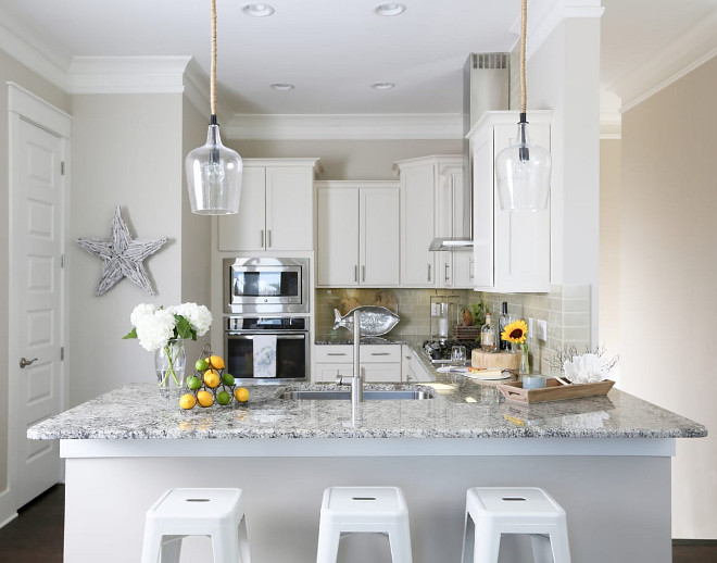 Small Kitchen Inspiration. The cabinets are wood and the designer painted them just a slightly warm white; Sherwin Williams SW 6385 Dover White. The backsplash is glass subway. Subway, to keep it casual but glass for the sparkle! Small White Kitchen with grey backsplash tile, white granite countertop and affordable lighting #SmallKitchen #SmallKitchens #SmallKitchenInspiration #KitchenInspiration #SmallWhiteKitchen #greybacksplashtile #whitegranite #countertop #affordablelighting #lighting JoAnn Regina Home