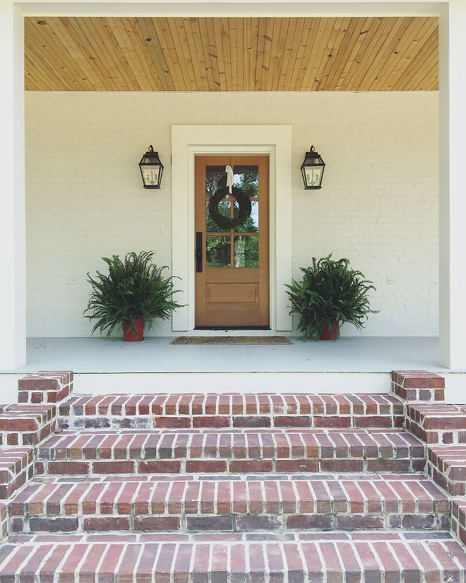 Farmhouse brick porch steps. Farmhouse brick porch step ideas. To bring in that Southern coastal feel, we had lanterns with the look of gas burning, and we used expose brick piers under the porches and tied them together with cream painted wood slats. Front Door: Simpson #7506 Thermal Sash Fir. Stain: Sherwin Williams Woodscapes in Covered Bridge. Door Trim: Emtek 451613 Rectangular Full Length Tubular Entrance Handleset with winchester interior knob - in flat black. Farmhouse brick porch steps. Farmhouse brick porch steps #Farmhouse #brickporchsteps #bricksteps #porchsteps Beautiful Homes of Instagram @theclevergoose