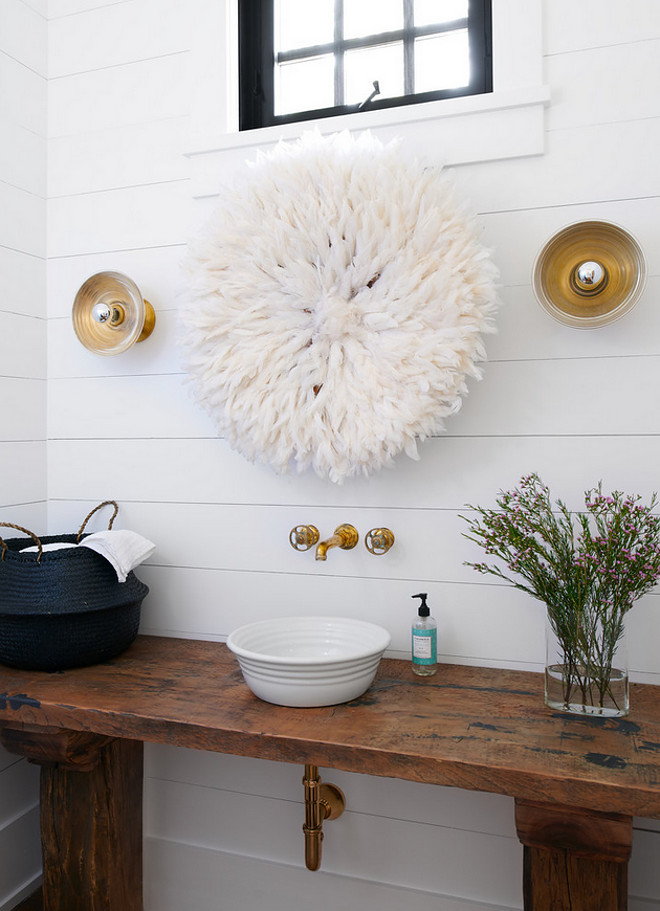 Farmhouse powder room boasts a shiplap wall lined with a white juju hat while gold sconces are placed over a repurposed console table topped with a white bowl sink and an antique brass faucet mounted on the wall. #farmhouse #powderroom #farmhousepowderroom #farmhousebathroom #bathroom Jennifer Worts Design Inc