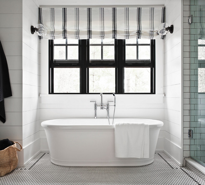 Modern Farmhouse Bathroom Shiplap. Black and white farmhouse bathroom with white hex tiled floor with black grout, freestanding bathtub, black windows dressed in a white and gray striped roman shade framed by white shiplap trim. Modern Farmhouse Bathroom Black Windows. Modern Farmhouse Bathroom Freestanding bath. Modern Farmhouse Bathroom Shades. Modern Farmhouse Bathroom Floor Tile #ModernFarmhouseBathroom #ModernFarmhouse #Bathroom #Shiplap #FarmhouseBathroomShiplap #FarmhouseBathroomBlackWindow #BlackWindows #FarmhouseBathroomFreestandingbath #Freestandingbath #FarmhouseBathroomShades #RomanshadesModern #FarmhouseBathroomFloorTile #FloorTile Jennifer Worts Design Inc