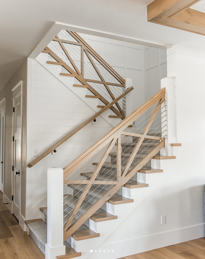Farmhouse Staircase. Farmhouse staircase features white oak railing and white oak crossed wood balusters and cable railing. Farmhouse staircase features white oak railing and white oak crossed wood balusters and cable railing. Walls feature a combination of shiplap and board and batten grid paneling #Farmhousestaircase #whiteoakstaircase #railing #whiteoakrailing #crossedwoodbalusters #cablerailing #shiplap #boardandbattengrid #paneling Millhaven Homes