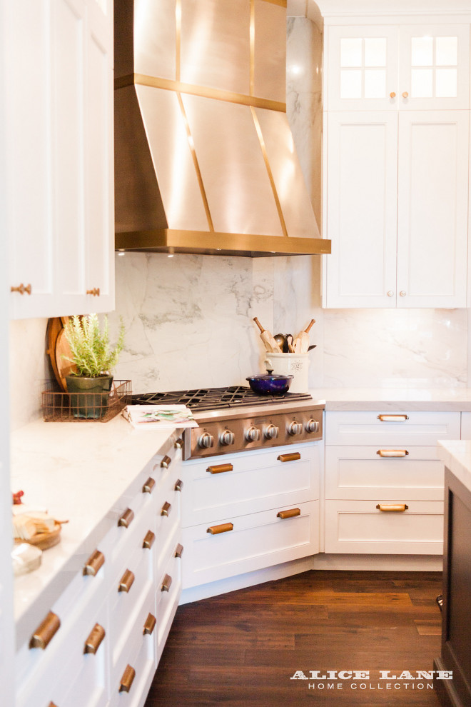 White kitchen with brass hardware, steel hood with brass strip and white quartzite countertop and full slap backsplash Alice Lane Home Collection