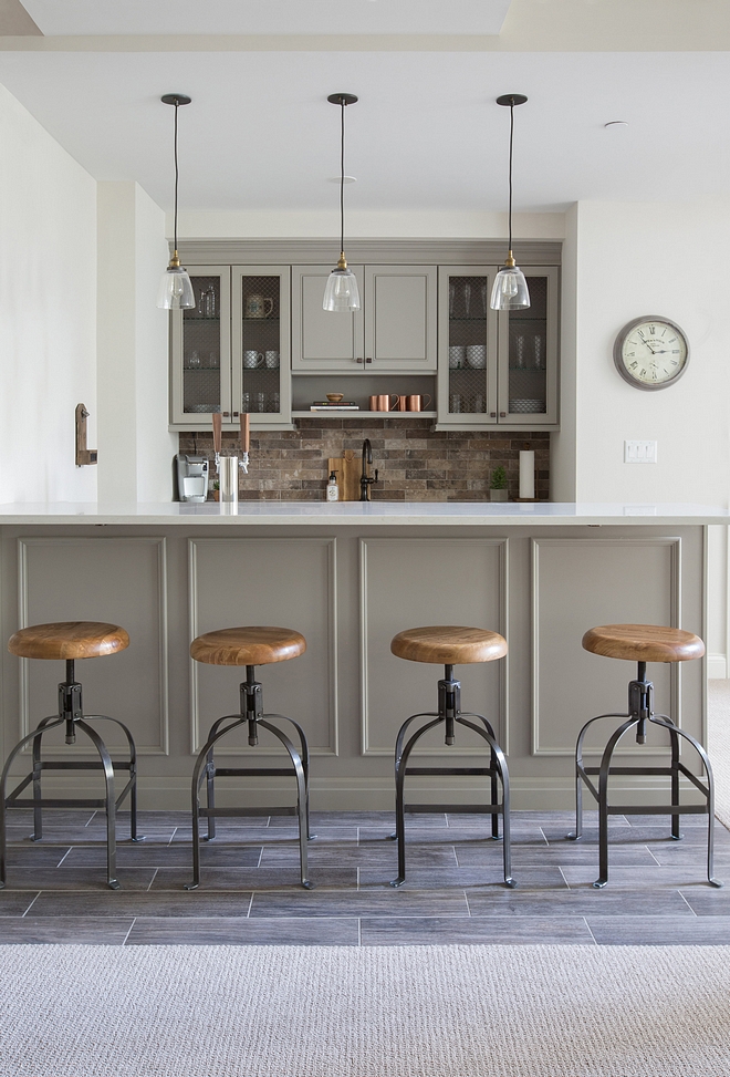 Basement features a grey bar, brick-style backsplash and wood-looking floor tile similar cabinet paint color Benjamin Moore Ozark Shadows