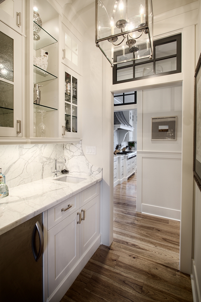 Butlers pantry with white cabinets painted in Benjamin Moore White paint color hardwood floors transom window above doorway and Statuario marble countertop and marble slab backsplash #butlerspantry