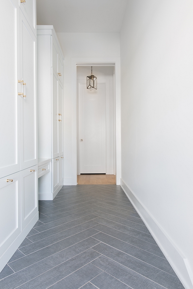 Mudroom features grey tile in a herringbone pattern and white cabinets