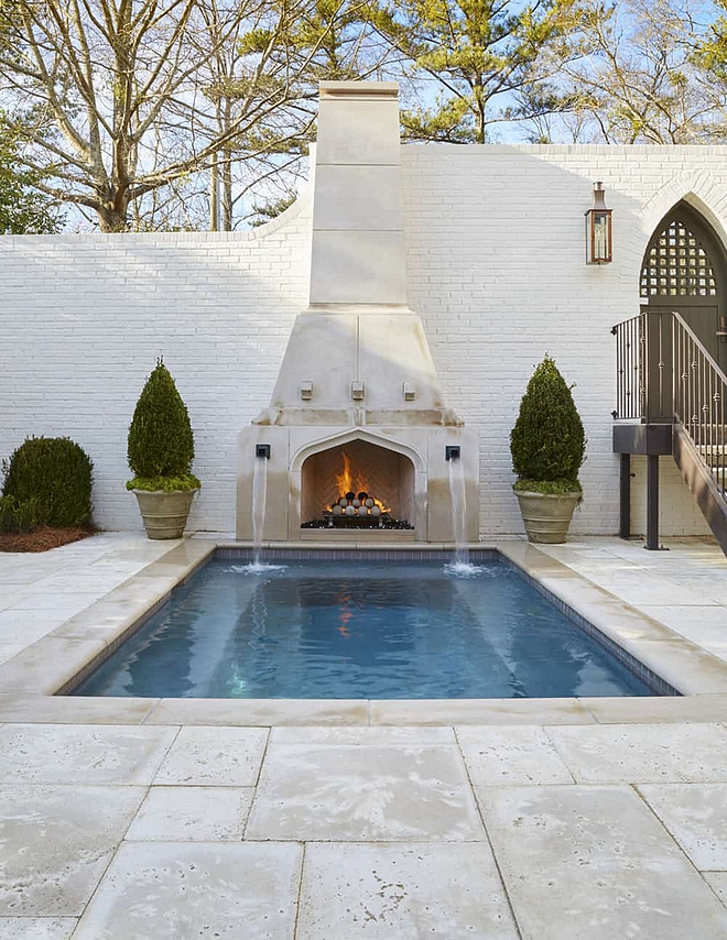 Pool with Fireplace Limestone pool surround The cocktail pool is flanked by two dramatic bronze fountain scuppers and a beautifully designed limestone fireplace adorned with limestone fireballs #Pool #poolFireplace #Limestone #poolsurround
